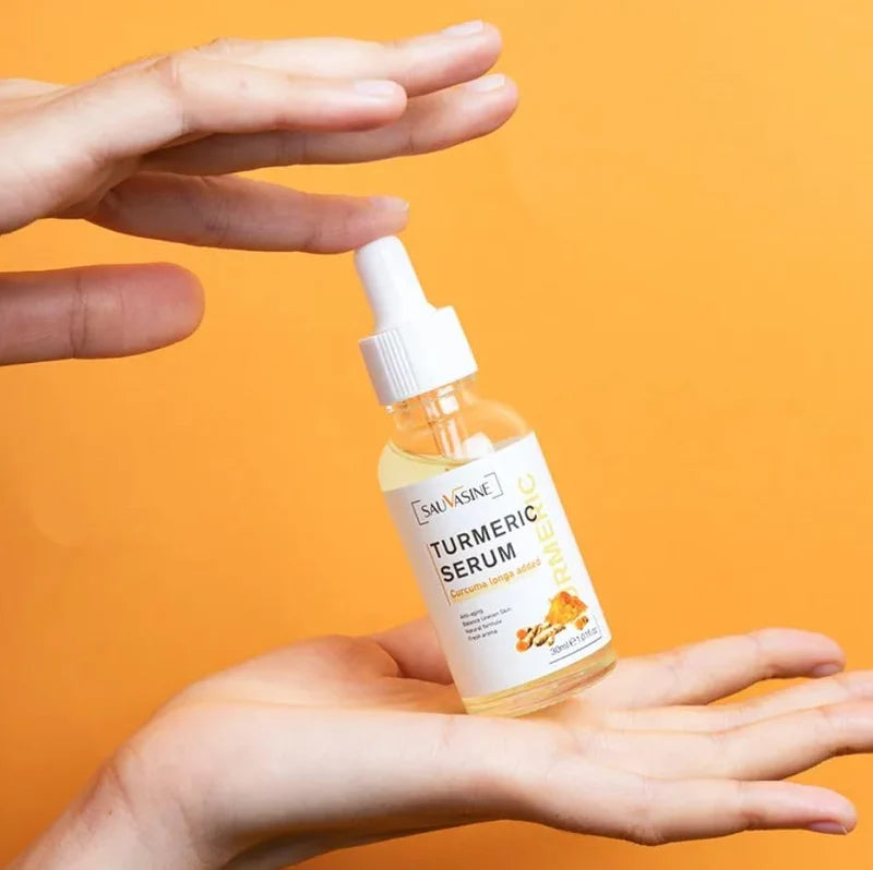 A clear dropper bottle of SAUVAGE Turmeric Serum resting inside a transparent round dish on a bright orange background, with small turmeric root pieces visible around it.